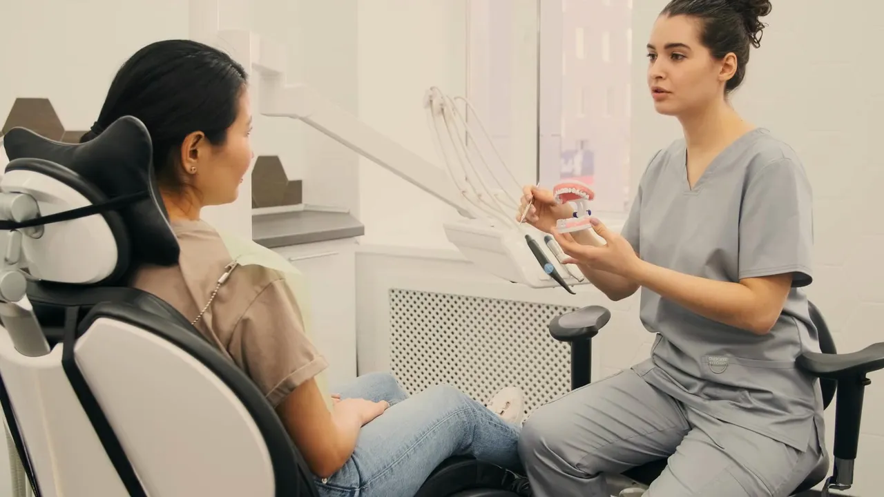 Medică stomatolog care îi explică unei paciente, pe un model dentar, ce urmează să facă